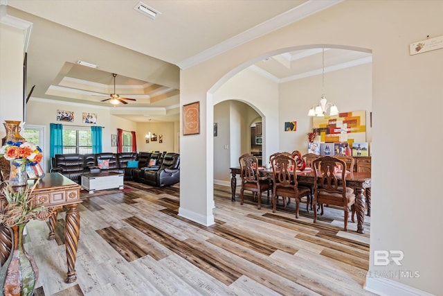 living room with ceiling fan with notable chandelier, ornamental molding, a tray ceiling, and light hardwood / wood-style floors