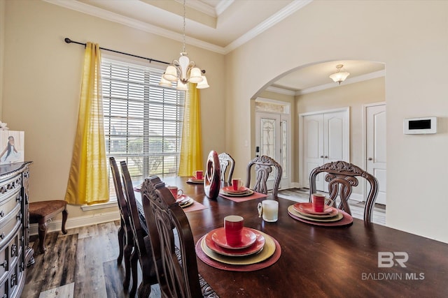 dining space with dark wood-type flooring, ornamental molding, and an inviting chandelier