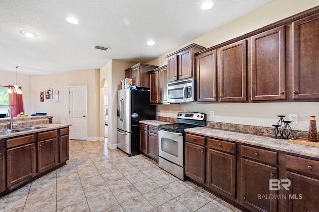 kitchen with pendant lighting, sink, stainless steel appliances, dark brown cabinetry, and light tile patterned flooring