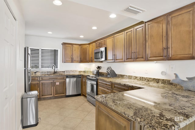 kitchen with stone counters, stainless steel appliances, a peninsula, visible vents, and brown cabinets