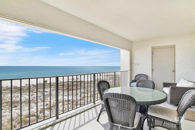 balcony with outdoor dining area, a water view, and a view of the beach