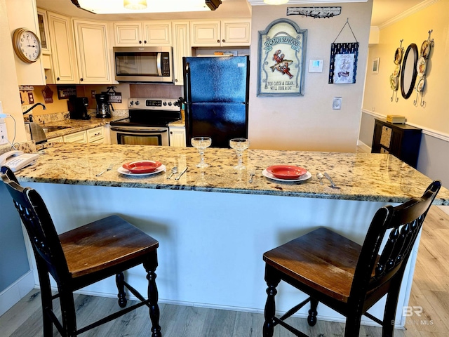 kitchen with appliances with stainless steel finishes, a sink, light wood-style flooring, and light stone counters