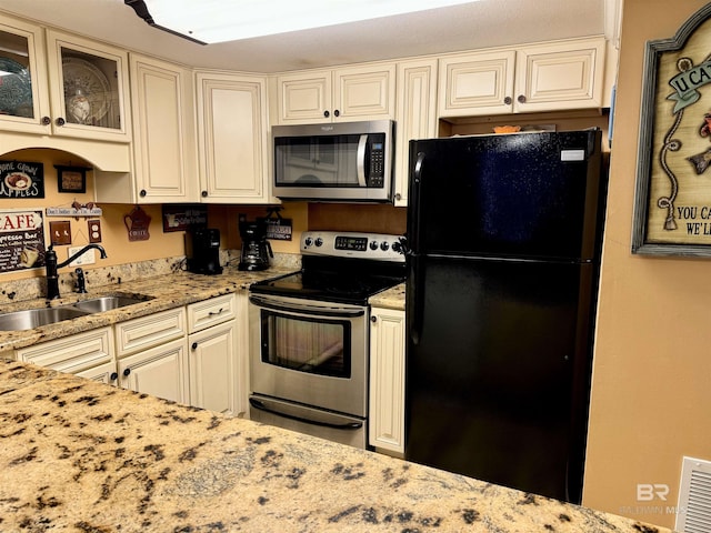 kitchen featuring light stone counters, stainless steel appliances, a sink, visible vents, and glass insert cabinets