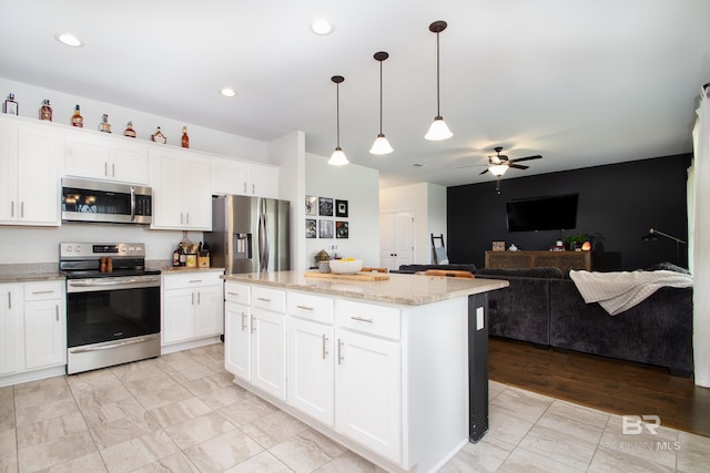 kitchen with ceiling fan, a kitchen island, pendant lighting, stainless steel appliances, and white cabinetry