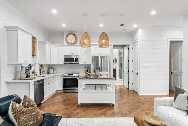 kitchen featuring hardwood / wood-style flooring, sink, white cabinetry, appliances with stainless steel finishes, and decorative light fixtures