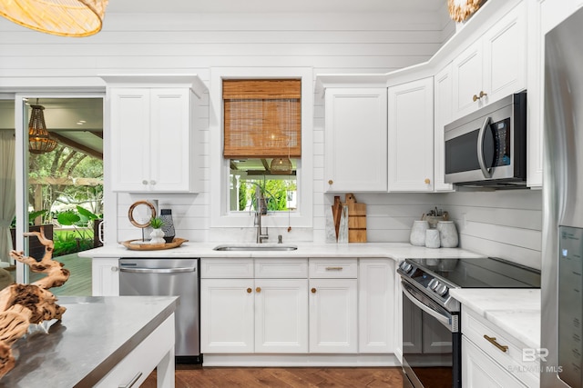 kitchen featuring a sink, appliances with stainless steel finishes, white cabinets, and wooden walls