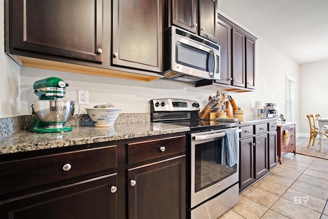 kitchen with dark brown cabinetry, stainless steel appliances, light tile patterned flooring, and stone countertops