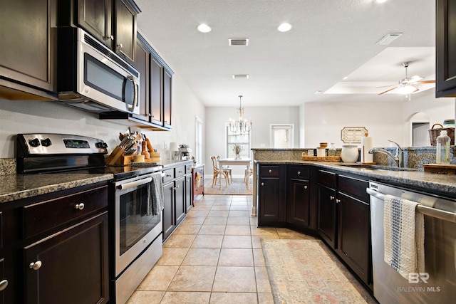 kitchen with stainless steel appliances, dark brown cabinetry, sink, ceiling fan with notable chandelier, and pendant lighting