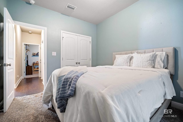 bedroom featuring dark wood-type flooring, a closet, lofted ceiling, and a textured ceiling