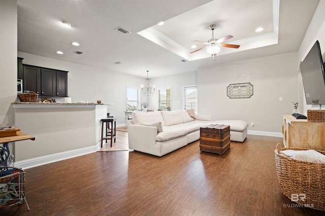 living room featuring a tray ceiling, dark hardwood / wood-style floors, and ceiling fan with notable chandelier