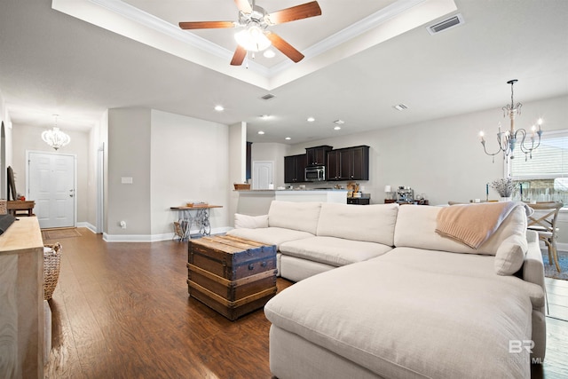 living room with ceiling fan with notable chandelier, a raised ceiling, dark hardwood / wood-style flooring, and ornamental molding