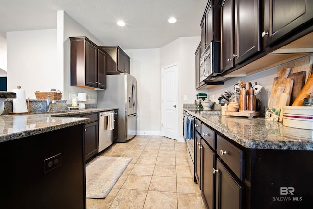 kitchen featuring light tile patterned flooring, dark brown cabinets, dark stone countertops, and appliances with stainless steel finishes