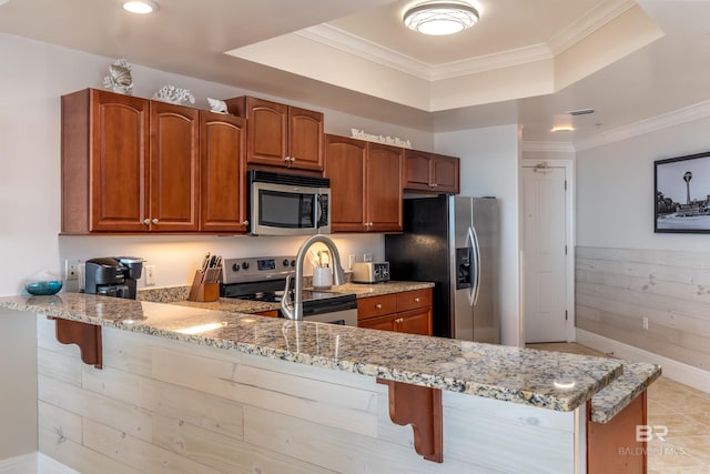 kitchen featuring stainless steel appliances, a breakfast bar, kitchen peninsula, light stone countertops, and a raised ceiling