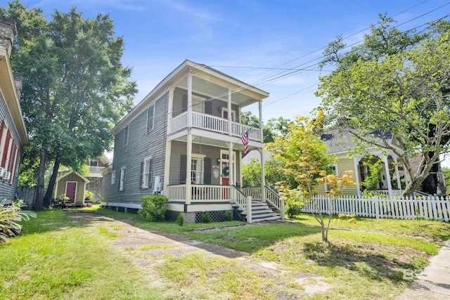 view of front of property with covered porch, a balcony, a front yard, and a storage shed