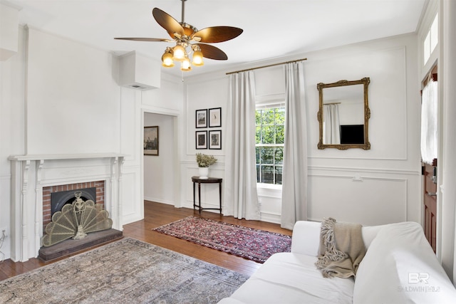 living room featuring a fireplace, ceiling fan, and dark wood-type flooring