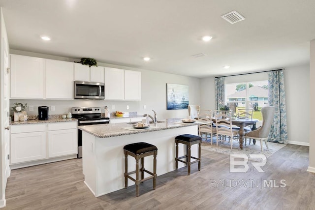 kitchen with stainless steel appliances, white cabinetry, a center island with sink, and light wood-type flooring