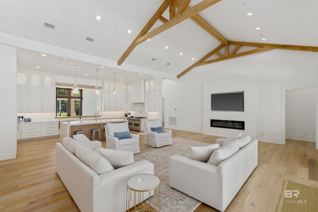 living room with beamed ceiling, light hardwood / wood-style floors, sink, and high vaulted ceiling