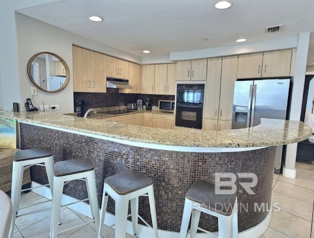 521 W Beach Blvd Unit 1703, Gulf Shores, AL 36542 - kitchen with under cabinet range hood, light stone counters, black appliances, and light brown cabinets