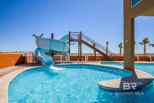 community pool featuring stairs, a water slide, and fence