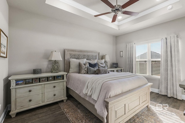 bedroom featuring dark hardwood / wood-style floors, ceiling fan, ornamental molding, and a tray ceiling