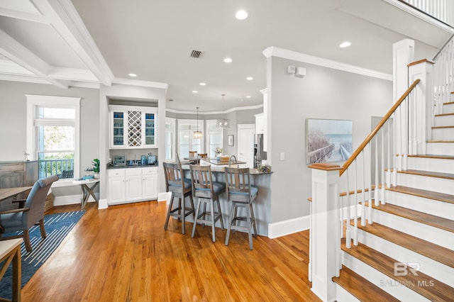 kitchen featuring light hardwood / wood-style floors, white cabinetry, hanging light fixtures, a kitchen breakfast bar, and ornamental molding