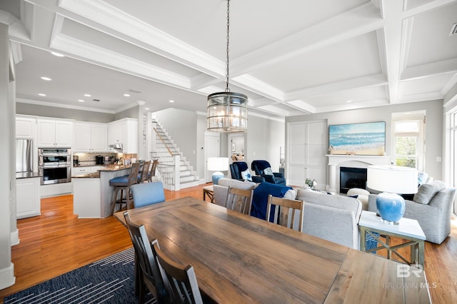 dining room featuring beam ceiling, light hardwood / wood-style floors, a chandelier, crown molding, and coffered ceiling