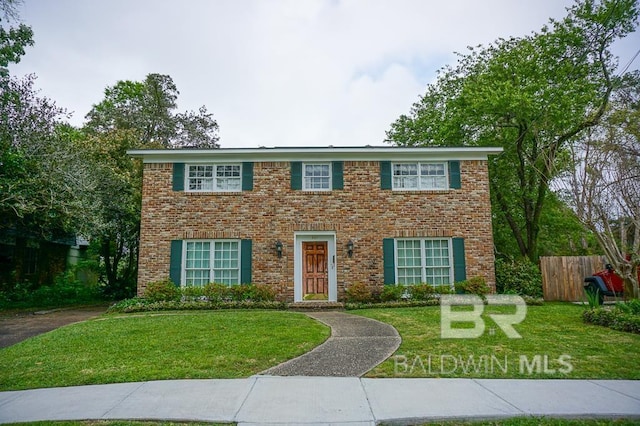 colonial inspired home featuring brick siding, a front lawn, and fence