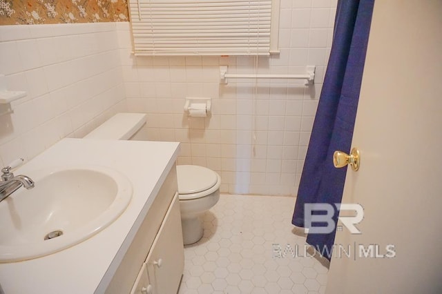 full bathroom with tile patterned flooring, toilet, vanity, tile walls, and wainscoting