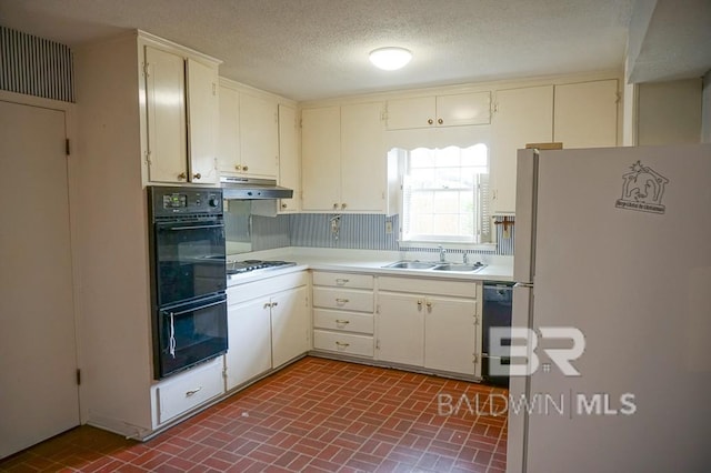 kitchen with a sink, black appliances, light countertops, under cabinet range hood, and brick patterned floor
