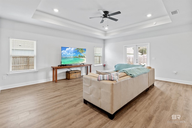 living room with french doors, crown molding, a raised ceiling, and light wood-type flooring