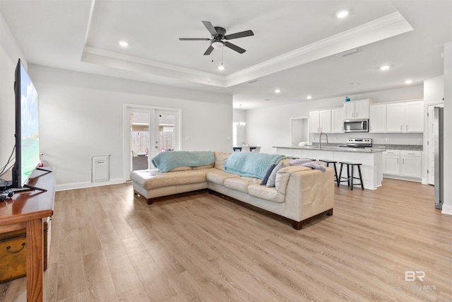 living room with sink, crown molding, light hardwood / wood-style flooring, ceiling fan, and a tray ceiling