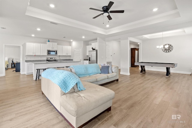 living room featuring crown molding, sink, a tray ceiling, and light wood-type flooring