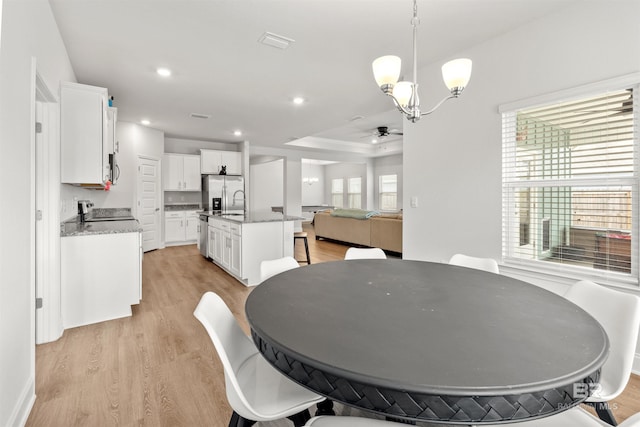 dining space featuring a raised ceiling, ceiling fan with notable chandelier, and light hardwood / wood-style floors