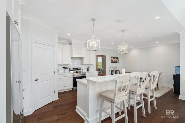 kitchen featuring premium range hood, stainless steel range with electric stovetop, hanging light fixtures, a kitchen island with sink, and white cabinets