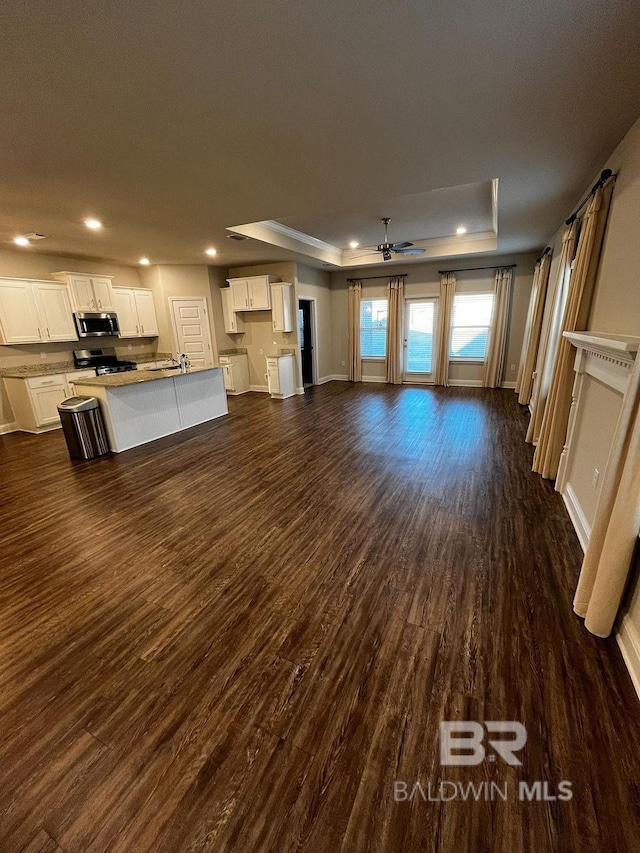 unfurnished living room with ceiling fan, dark hardwood / wood-style floors, and a raised ceiling