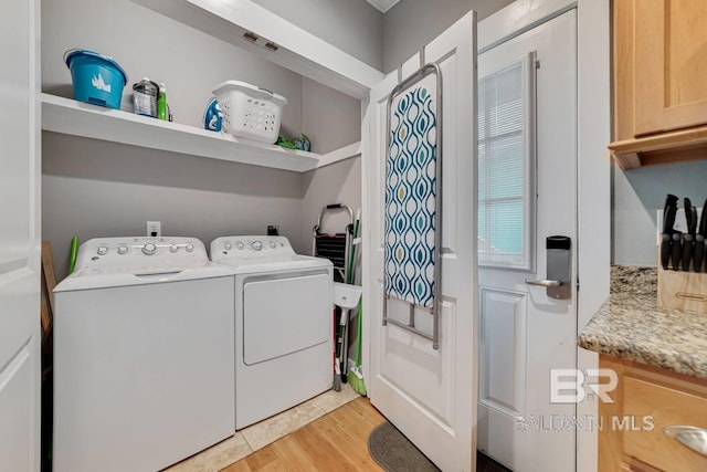 washroom with light hardwood / wood-style flooring, washing machine and dryer, and cabinets