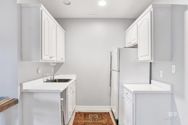 kitchen with white refrigerator, white cabinetry, and sink