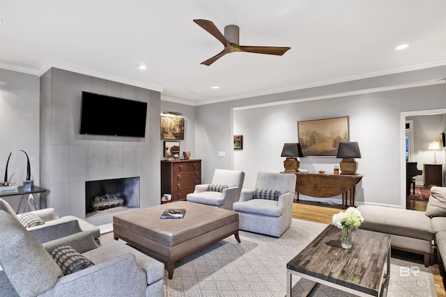 living room featuring light wood-type flooring, ceiling fan, crown molding, and a tiled fireplace