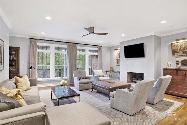 living room with ceiling fan, light hardwood / wood-style floors, ornamental molding, and a fireplace