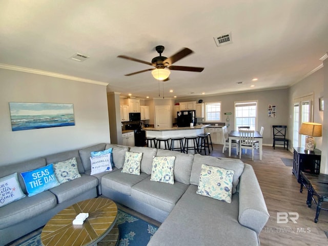 living room with visible vents, wood finished floors, and ornamental molding