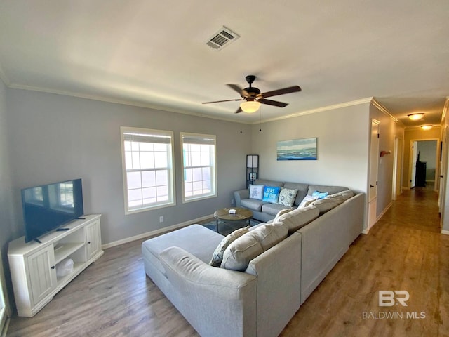 living room with ornamental molding, light wood-type flooring, visible vents, and a ceiling fan