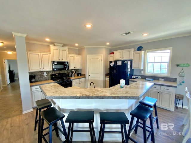 kitchen with a kitchen island with sink, visible vents, light countertops, backsplash, and black appliances