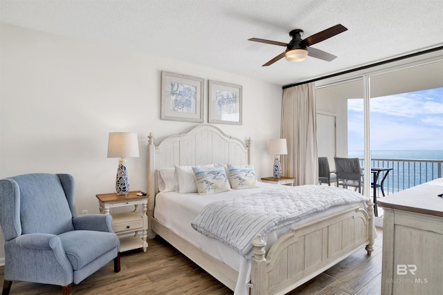 bedroom featuring a water view, dark wood-style floors, floor to ceiling windows, and access to exterior