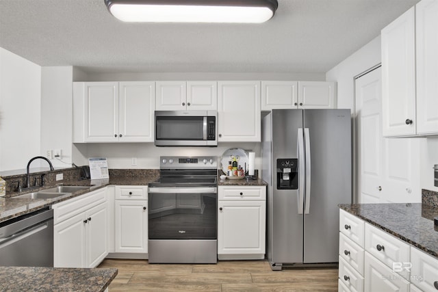 kitchen with dark stone countertops, stainless steel appliances, a sink, white cabinetry, and light wood-type flooring