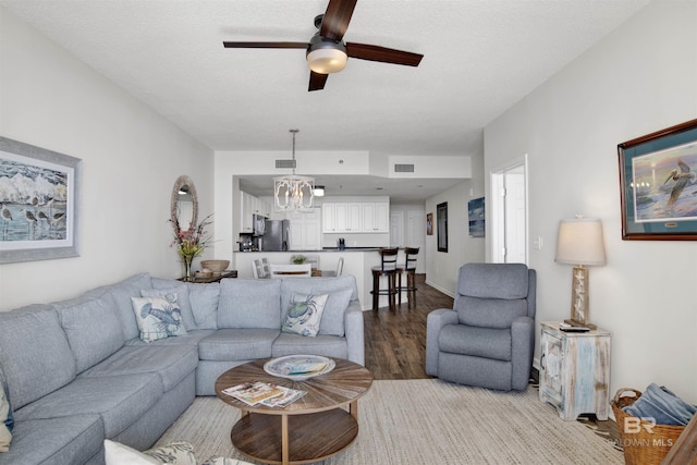 living area featuring visible vents, ceiling fan with notable chandelier, light wood finished floors, and a textured ceiling