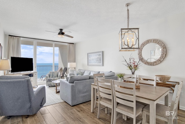 living area featuring ceiling fan with notable chandelier, a textured ceiling, a wall of windows, and wood finished floors