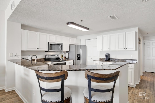 kitchen with dark stone counters, visible vents, white cabinets, stainless steel appliances, and a peninsula