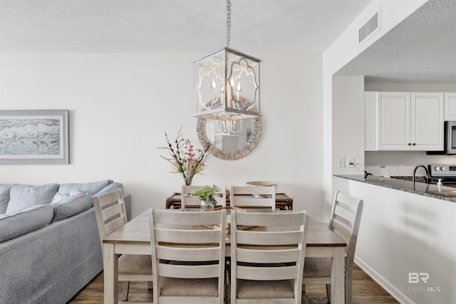 dining area featuring visible vents, baseboards, dark wood finished floors, a notable chandelier, and a textured ceiling