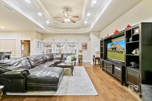 living room featuring a raised ceiling, crown molding, light hardwood / wood-style flooring, and ceiling fan