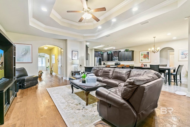 living room featuring a raised ceiling, ceiling fan with notable chandelier, light hardwood / wood-style flooring, and ornamental molding